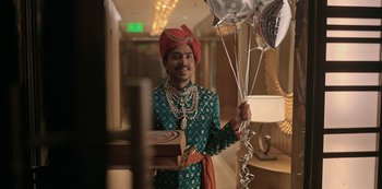 Movie still from “The White Tiger” (2021), directed by Ramin Bahrani – A man wearing a turban and holding a bunch of balloons; Wide shot, Low angle