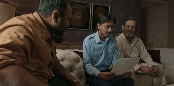 Movie still from “The White Tiger” (2021), directed by Ramin Bahrani – A group of men sitting on a couch looking at papers; Medium shot, Over the shoulder angle