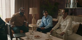 Movie still from “The White Tiger” (2021), directed by Ramin Bahrani – A group of people sitting around a table with plates of food on top of it; Medium shot, High angle