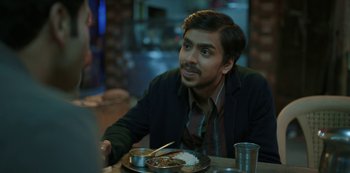 Movie still from “The White Tiger” (2021), directed by Ramin Bahrani – A man sitting in front of a plate of food; Close Up shot, Over the shoulder angle