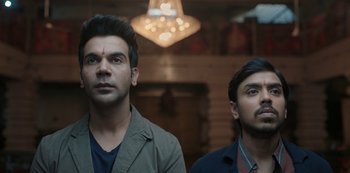 Movie still from “The White Tiger” (2021), directed by Ramin Bahrani – Two men standing next to each other in front of a chandelier; Close Up shot, Low angle