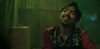 Movie still from “The White Tiger” (2021), directed by Ramin Bahrani – A man in a red shirt is smiling; Close Up shot, High angle