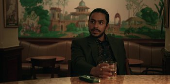 Movie still from “The White Tiger” (2021), directed by Ramin Bahrani – A man sitting at a table with a glass of water; Medium shot, Low angle