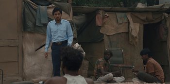 Movie still from “The White Tiger” (2021), directed by Ramin Bahrani – A man standing in front of a man sitting on a chair; Medium shot, Over the shoulder angle