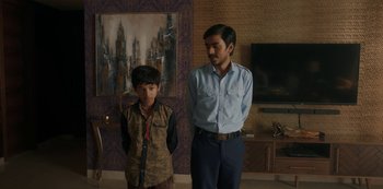 Movie still from “The White Tiger” (2021), directed by Ramin Bahrani – A man standing next to a young boy in a room; Medium shot, Over the shoulder angle