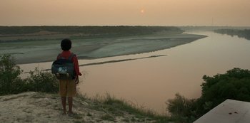 Movie still from “The White Tiger” (2021), directed by Ramin Bahrani – A person standing on a hill looking at a body of water; Wide shot, High angle