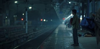 Movie still from “The White Tiger” (2021), directed by Ramin Bahrani – A man standing on a platform waiting for a train; Wide shot, Low angle