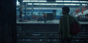 Movie still from “The White Tiger” (2021), directed by Ramin Bahrani – A man standing on a train platform next to train tracks; Wide shot, Low angle