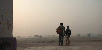Movie still from “The White Tiger” (2021), directed by Ramin Bahrani – Two people standing on a dirt road holding hands; Wide shot, Low angle