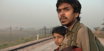 Movie still from “The White Tiger” (2021), directed by Ramin Bahrani – A man and a boy standing next to each other on the side of a road; Close Up shot, Low angle