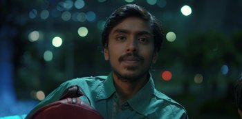 Movie still from “The White Tiger” (2021), directed by Ramin Bahrani – A young man holding a skateboard in his hands; Close Up shot, Low angle