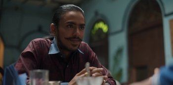 Movie still from “The White Tiger” (2021), directed by Ramin Bahrani – A person sitting at a table; Close Up shot, Low angle