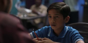 Movie still from “The White Tiger” (2021), directed by Ramin Bahrani – A young boy is holding a red pencil in his hand; Close Up shot, Over the shoulder angle
