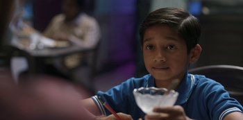 Movie still from “The White Tiger” (2021), directed by Ramin Bahrani – A young boy holding a glass of water in his hand; Close Up shot, Over the shoulder angle