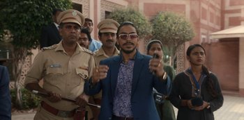 Movie still from “The White Tiger” (2021), directed by Ramin Bahrani – A man in a blue suit and sunglasses holding a cell phone; Medium shot, Low angle