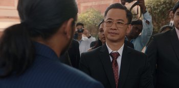 Movie still from “The White Tiger” (2021), directed by Ramin Bahrani – A man in a suit and tie standing in front of a group of people; Close Up shot, Over the shoulder angle