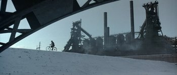 Movie still from “Road to Perdition” (2002), directed by Sam Mendes – A man riding a bike on top of a snow covered slope; Extreme Wide shot, High angle
