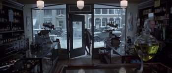 Movie still from “Road to Perdition” (2002), directed by Sam Mendes – A person walking through a store front window in the snow; Wide shot, High angle