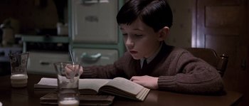 Movie still from “Road to Perdition” (2002), directed by Sam Mendes – A young boy reading a book at a table; Close Up shot, High angle