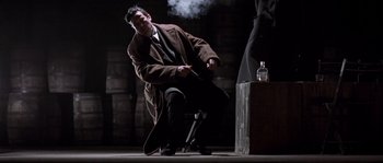 Movie still from “Road to Perdition” (2002), directed by Sam Mendes – A man sitting on a chair in a dark room; Medium shot, Low angle