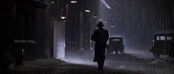 Movie still from “Road to Perdition” (2002), directed by Sam Mendes – A man walking in the rain with a hat on; Wide shot, Low angle