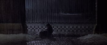 Movie still from “Road to Perdition” (2002), directed by Sam Mendes – A person sitting on the ground in front of an iron gate; Wide shot, High angle