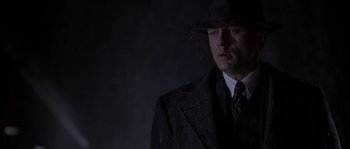 Movie still from “Road to Perdition” (2002), directed by Sam Mendes – A man in a suit and hat standing in the rain; Close Up shot, Low angle