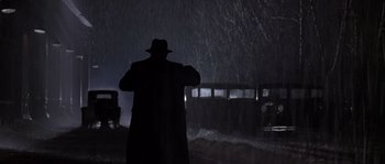 Movie still from “Road to Perdition” (2002), directed by Sam Mendes – A man standing in the rain in front of a bus; Wide shot, Low angle