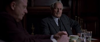 Movie still from “Road to Perdition” (2002), directed by Sam Mendes – An older man wearing a suit and tie sitting in front of another man in a suit; Medium shot, Over the shoulder angle
