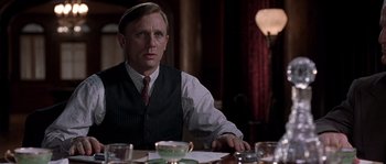 Movie still from “Road to Perdition” (2002), directed by Sam Mendes – A man sitting at a dinner table in front of a lamp; Medium shot, Over the shoulder angle