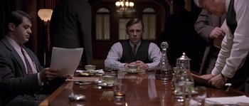 Movie still from “Road to Perdition” (2002), directed by Sam Mendes – A man sitting at a table with a cup of tea; Medium shot, Low angle