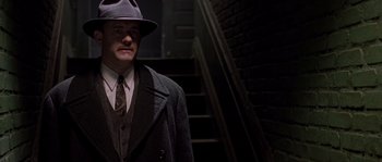Movie still from “Road to Perdition” (2002), directed by Sam Mendes – A man wearing a hat and a suit standing in a dark room; Medium shot, Low angle