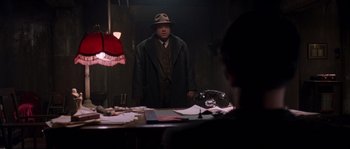 Movie still from “Road to Perdition” (2002), directed by Sam Mendes – A man standing in front of a table in a room; Medium shot, Over the shoulder angle