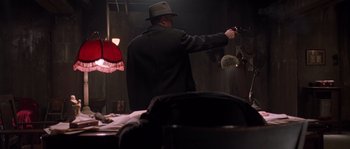 Movie still from “Road to Perdition” (2002), directed by Sam Mendes – A man holding a gun in a room with lights on; Medium shot, High angle
