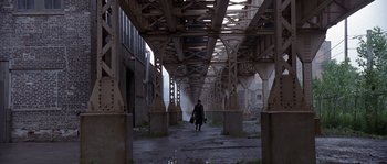 Movie still from “Road to Perdition” (2002), directed by Sam Mendes – A person walking down a street under a bridge; Extreme Wide shot, High angle