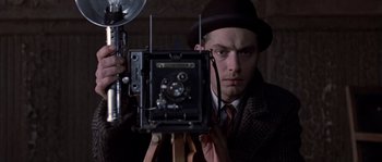 Movie still from “Road to Perdition” (2002), directed by Sam Mendes – A man in a suit and hat holding a camera; Close Up shot, Low angle