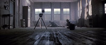 Movie still from “Road to Perdition” (2002), directed by Sam Mendes – A man sitting on the ground in an abandoned building; Wide shot, High angle