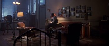 Movie still from “Road to Perdition” (2002), directed by Sam Mendes – A man sitting on top of a couch in a living room; Wide shot, High angle