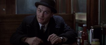Movie still from “Road to Perdition” (2002), directed by Sam Mendes – A man wearing a hat and a coat sitting at a table; Close Up shot, Low angle