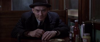 Movie still from “Road to Perdition” (2002), directed by Sam Mendes – A man sitting at a wooden table wearing a hat; Close Up shot, Low angle