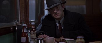 Movie still from “Road to Perdition” (2002), directed by Sam Mendes – A man sitting at a dinner table wearing a hat; Medium shot, Over the shoulder angle