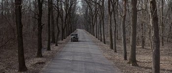 Movie still from “Road to Perdition” (2002), directed by Sam Mendes – An old car driving down a tree - lined road; Extreme Wide shot, High angle