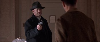 Movie still from “Road to Perdition” (2002), directed by Sam Mendes – A man holding a gun in front of another man in a suit; Medium shot, Over the shoulder angle