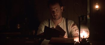 Movie still from “Road to Perdition” (2002), directed by Sam Mendes – A man sitting at a table looking down at a book; Close Up shot, Low angle