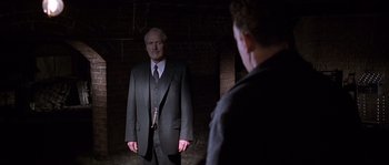 Movie still from “Road to Perdition” (2002), directed by Sam Mendes – A man in a suit and tie standing in front of another man in a suit and tie; Medium shot, Over the shoulder angle