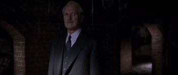 Movie still from “Road to Perdition” (2002), directed by Sam Mendes – An older man in a suit and tie in a dark room; Medium shot, Low angle