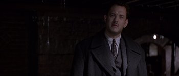 Movie still from “Road to Perdition” (2002), directed by Sam Mendes – A man wearing a suit and tie standing in a dark room; Close Up shot, Low angle