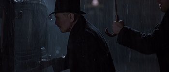 Movie still from “Road to Perdition” (2002), directed by Sam Mendes – A man in a black hat and a black coat holding an umbrella in the rain; Close Up shot, Over the shoulder angle
