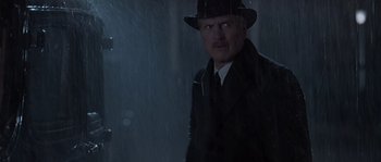 Movie still from “Road to Perdition” (2002), directed by Sam Mendes – A man wearing a hat and a suit standing in the rain; Medium shot, Low angle