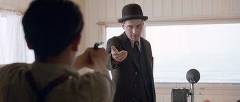 Movie still from “Road to Perdition” (2002), directed by Sam Mendes – A man in a suit and a top hat holding a camera; Medium shot, Low angle